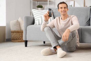Uzaktan kumandalı genç adam evde yerde oturuyor.
