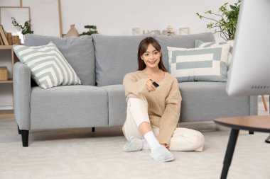 Evde yerde televizyon izleyen genç bir kadın.