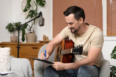 Evdeki koltuğa gitar notaları yazan genç ve mutlu bir besteci.