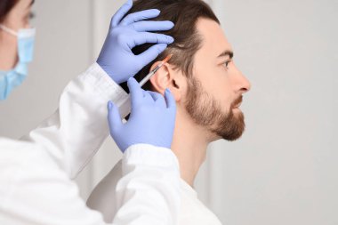 Genç adam trikoloğun ofisinde saç büyütme iğnesi yaptırıyor.