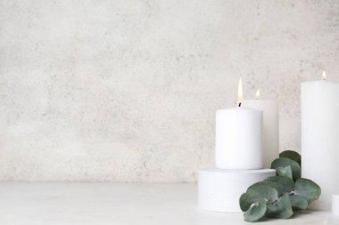 Beyaz arkaplanda yanan mumlar ve okaliptüs dallarıyla dekoratif podyum