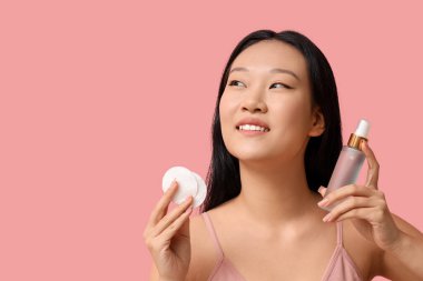 Pamuk pedleri ve pembe arka planda bir şişe cilt ürünüyle genç Asyalı kadın, yakın plan.