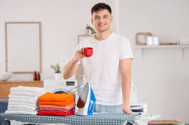 Demiri olan yakışıklı genç bir adam, evde bir sürü kıyafet ve kahve var.