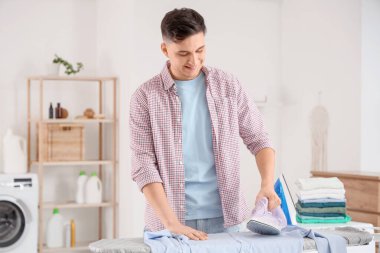 Evde ütü yapan bir yığın temiz elbisesi olan yakışıklı genç adam.