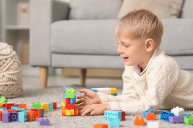 Mutlu küçük çocuk evde renkli oyuncak tuğlalarla oynuyor.