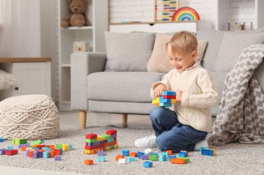 Mutlu küçük çocuk evde renkli oyuncak tuğlalarla oynuyor.