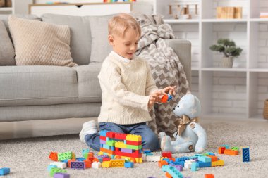 Mutlu küçük çocuk evde renkli oyuncak tuğlalar ve oyuncak ayıyla oynuyor.