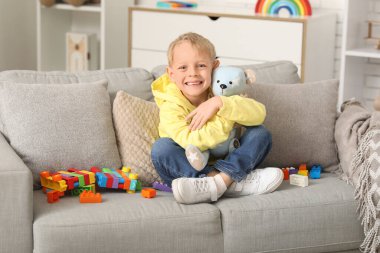 Evdeki kanepede renkli oyuncak tuğlalarla ve oyuncak ayılarla oynayan mutlu küçük çocuk.