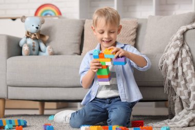 Mutlu küçük çocuk evde renkli oyuncak tuğlalarla oynuyor.
