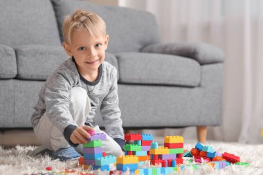 Mutlu küçük çocuk evde renkli oyuncak tuğlalarla oynuyor.