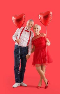 Kırmızı arka planda kalp şeklinde balonları olan mutlu, olgun bir çift. Sevgililer Günü kutlaması