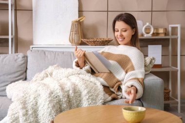Kış günü evde sıcak ekose kitap okuyan genç bir kadın.