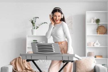 Kulaklıklı genç bir kadın evde sentezleyici çalıyor.