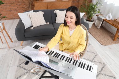 Mutlu genç kadın evde sentezleyici oynuyor.