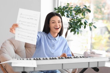 Evdeki koltukta sentezleyici çalan not kağıdıyla genç bir kadın.