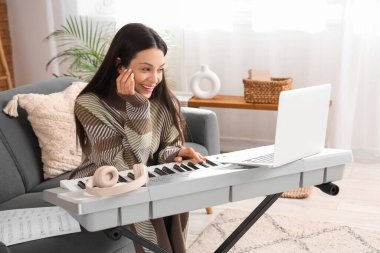 Evdeki kanepede sentezleyici çalan güzel genç bir kadın.