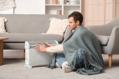 Evde elektrikli konteyner ısıtıcısının yanında ekose ısıtmalı genç bir adam var.