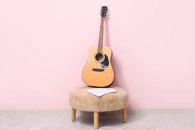 Renk duvarının yanındaki pouf 'ta akustik gitar ve müzik kağıtları