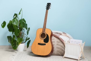 Akustik gitar, müzik kağıtları, pouf ve ev bitkisi renk duvarının yanında.