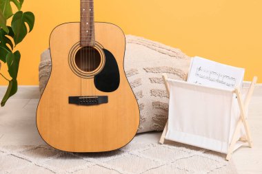 Akustik gitar, müzik kağıtları ve pouf renkli duvarın yanında.