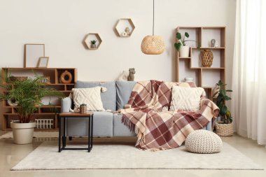 Oturma odasının iç tarafında yumuşak kareli battaniye, puf ve sehpa.