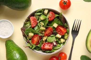 Sarı arka planda kiraz domatesli bir kâse lezzetli avokado salatası.