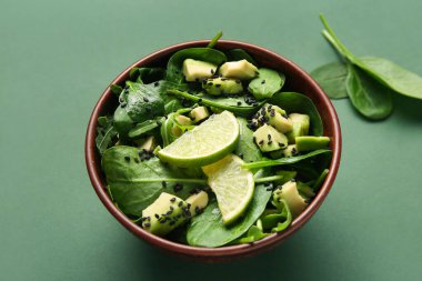 Bir kase lezzetli avokado salatası, ıspanak yaprakları ve yeşil arka planda limon.