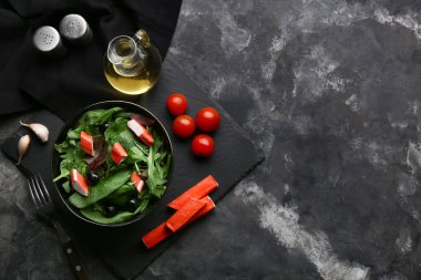 Yengeç çubuklu bir tabak salata, ıspanak, siyah zeytin ve gri grunge arka planda malzemeler.