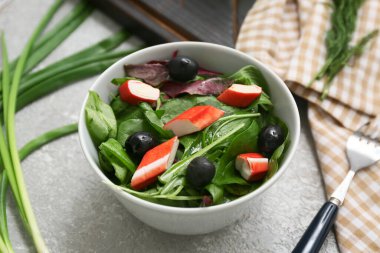 Bir kase salata ile yengeç çubuğu, ıspanak ve gri grunge arka planda siyah zeytin.