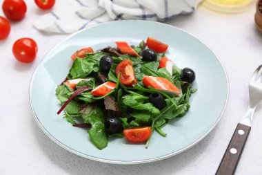 Yengeç çubuklu bir tabak salata, ıspanak, siyah zeytin ve beyaz arka planda domates.