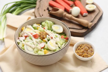 Yengeç saplı bir kase salata, buzdağı yaprakları, mısır, bıldırcın yumurtası ve beyaz arka planda salatalık.