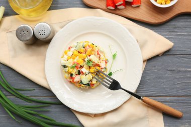Yengeç sopalı bir tabak salata, gri ahşap arka planda mısır ve salatalık