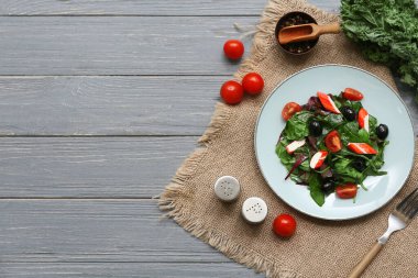 Yengeç çubuklu salata, ıspanak, siyah zeytin ve domatesler gri ahşap arka planda.