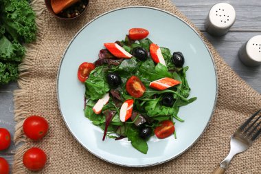 Yengeç çubuklu salata, ıspanak, siyah zeytin ve domatesler gri ahşap arka planda.