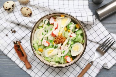 Bir kase salata ile yengeç sopası, mısır ve salatalık gri ahşap arka planda.