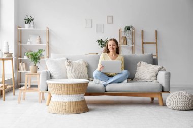 oturma odasında kanepede otururken dizüstü kullanarak güzel bir genç kadın