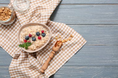 Peçete, lezzetli yulaf ezmeli kase, gri ahşap arka planda chia tohumları ve meyveler.
