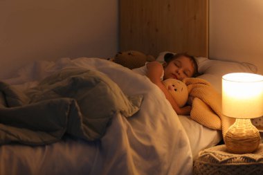 Örgü ören oyuncak tavşancığı olan sevimli küçük kız geceleri yatak odasında uyuyor.