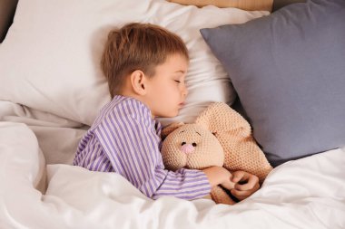 Örgü örmüş oyuncak tavşancığı olan şirin bir çocuk. Yatak odasında uyuyor.