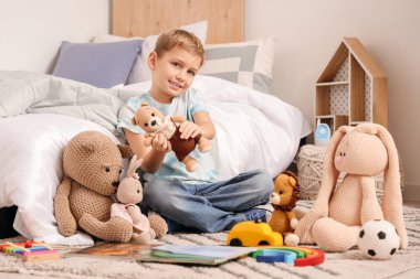 Yatak odasındaki halıda oyuncakları olan şirin bir çocuk.