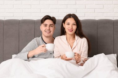 Genç çift yatakta kahve içiyor.