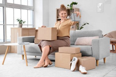 Paket kutuları ve yeni çantasıyla evdeki kanepede oturan genç kadın.