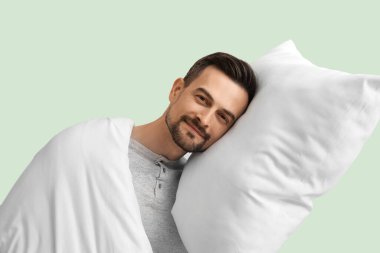 Yeşil arka planda yumuşak yastıklı ve battaniyeli yakışıklı bir adam.