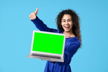Mutlu Afro-Amerikalı kadın elinde mavi arka planda yeşil ekranlı modern bir laptop tutuyor. Tasarım için model