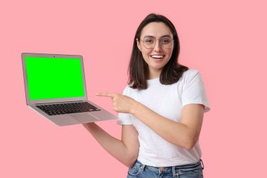 Pembe arka planda yeşil ekranlı dizüstü bilgisayarı gösteren genç bir kadın. Tasarım için model