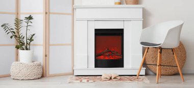 Koltuğu, perdesi, şöminesi ve halıdaki terlikleri olan oturma odasının içinde.