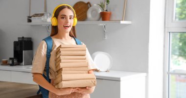 Kulaklıklı ve mutfakta bir sürü kitabı olan bir kız öğrenci.