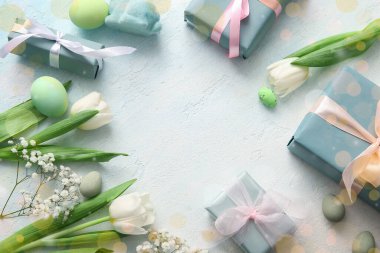 Paskalya yumurtalarından, çiçeklerden ve açık arkaplanda hediye kutularından yapılmış çerçeve