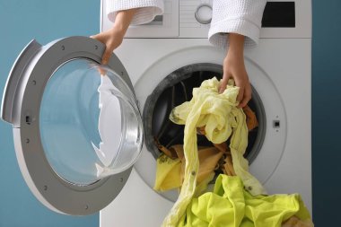 Woman putting dirty clothes in washing machine with black mold at home clipart