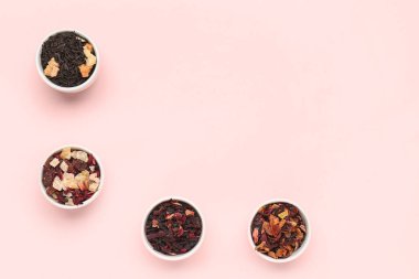 Pembe arka planda farklı kurutulmuş meyve çaylarıyla dolu kaseler.